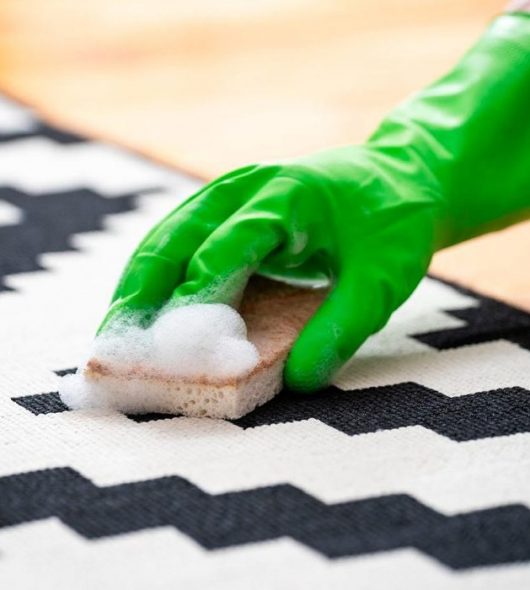female hand in green rubber glove wash floor carpet with soap foam and sponge in apartment room, cropped shot, cleaning service concept